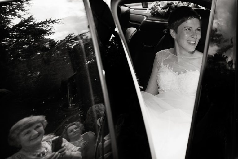 bride in wedding car with reflections of guests