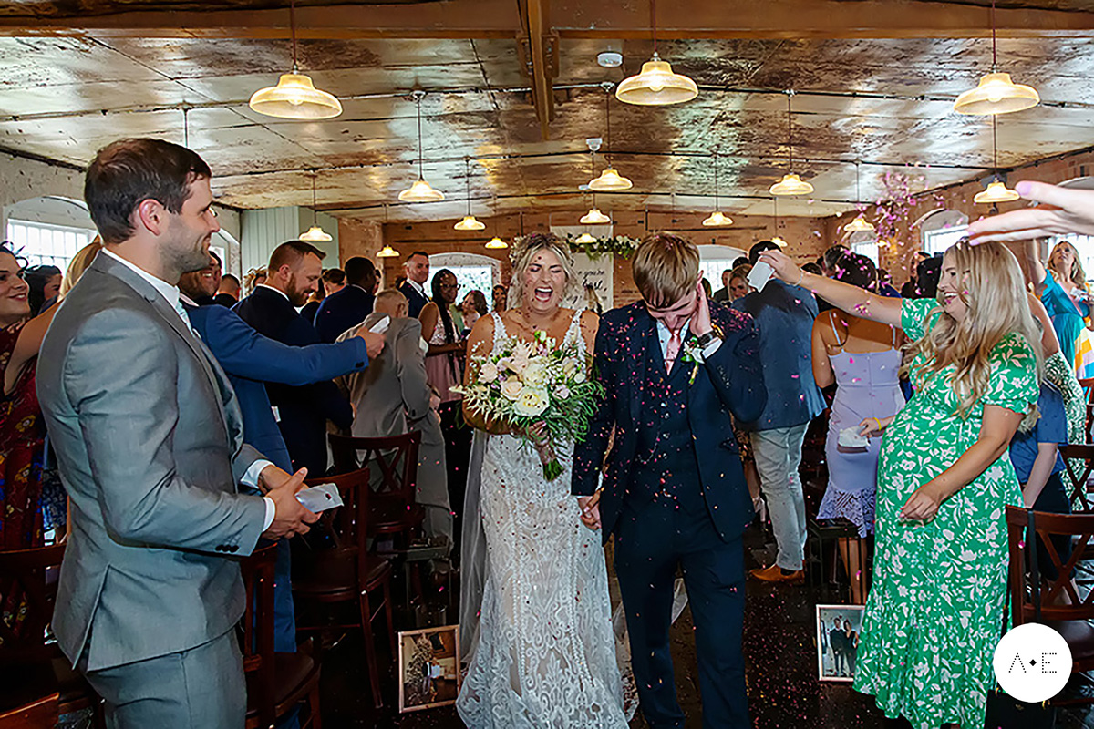 bride and groom walking down aisley guest throwing confetti captured by documentary wedding photographer Alison Edwards